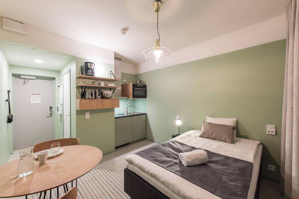 A compact room with a bed, a small dining table, and a kitchenette.