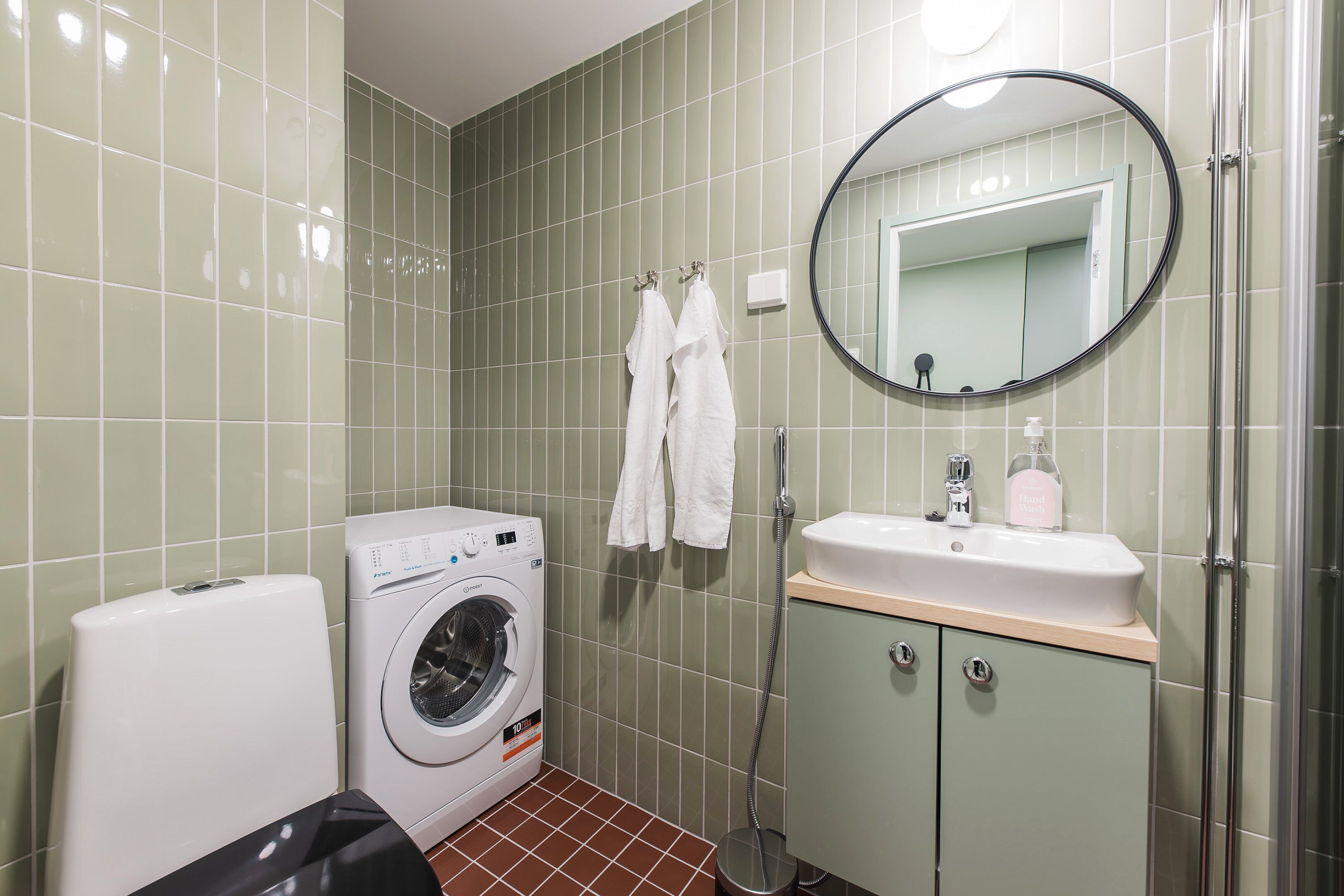 Un baño pequeño con lavadora, lavamanos con espejo y cabina de ducha.