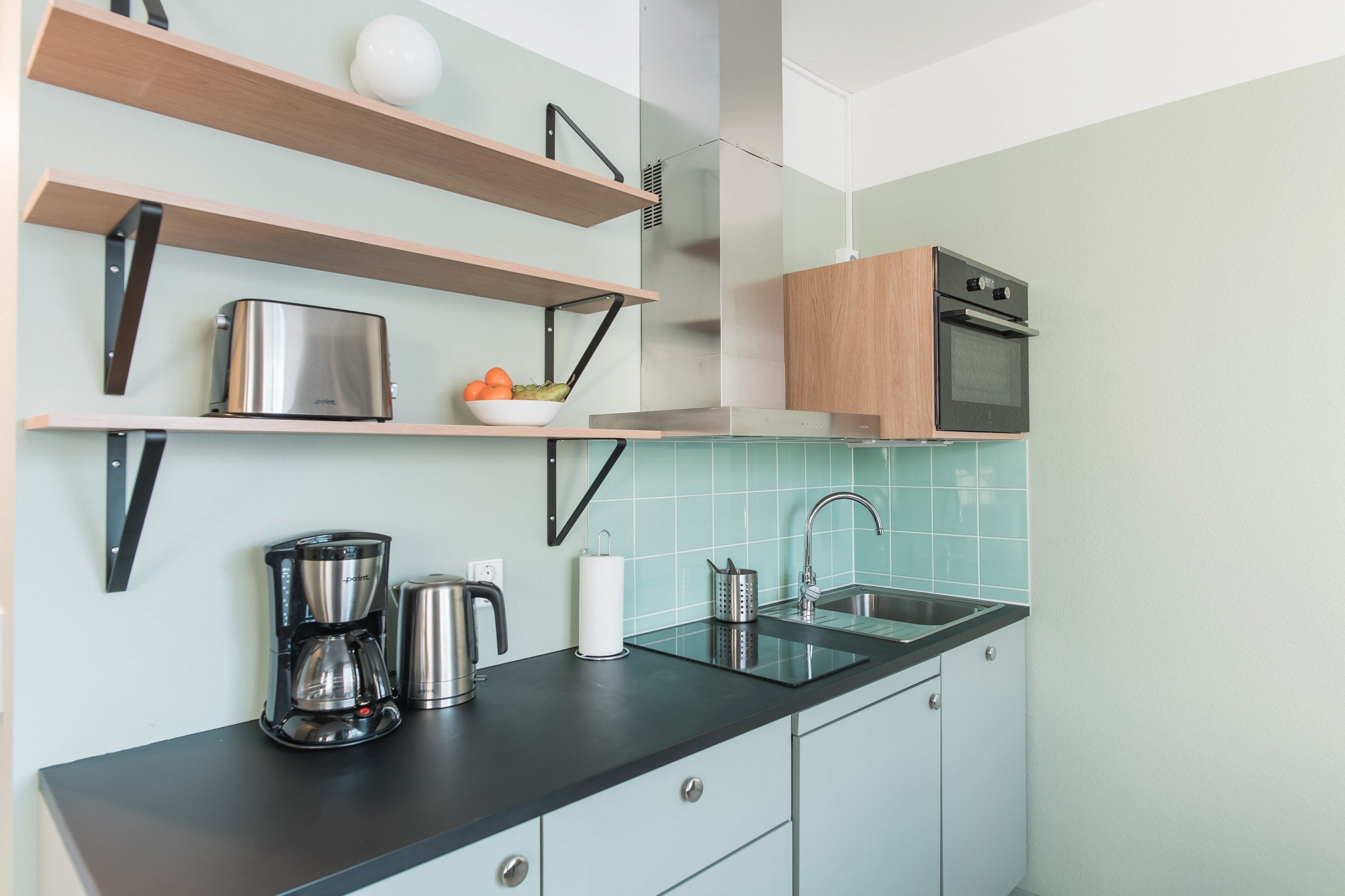 A modern kitchen with wooden shelves, a stainless steel toaster, a coffee maker, and a sink.