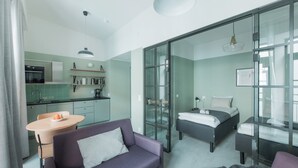 Una habitación moderna con sofá, cama, separador de vidrio, zona de cocina y mesa de comedor.