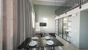Un comedor con una mesa dispuesta para cuatro, un televisor en la pared y una escalera que sube a un nivel superior.