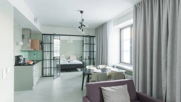 Un espacio habitable moderno y abierto con zona de comedor, kitchenette y un amplio ventanal con cortinas.