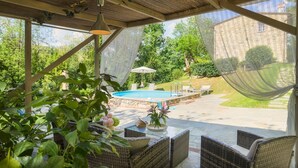 A covered outdoor area with a pool, wicker furniture, and a view of a stone building. - Ai Due Cuori 4, Emma Villas (Capannori)