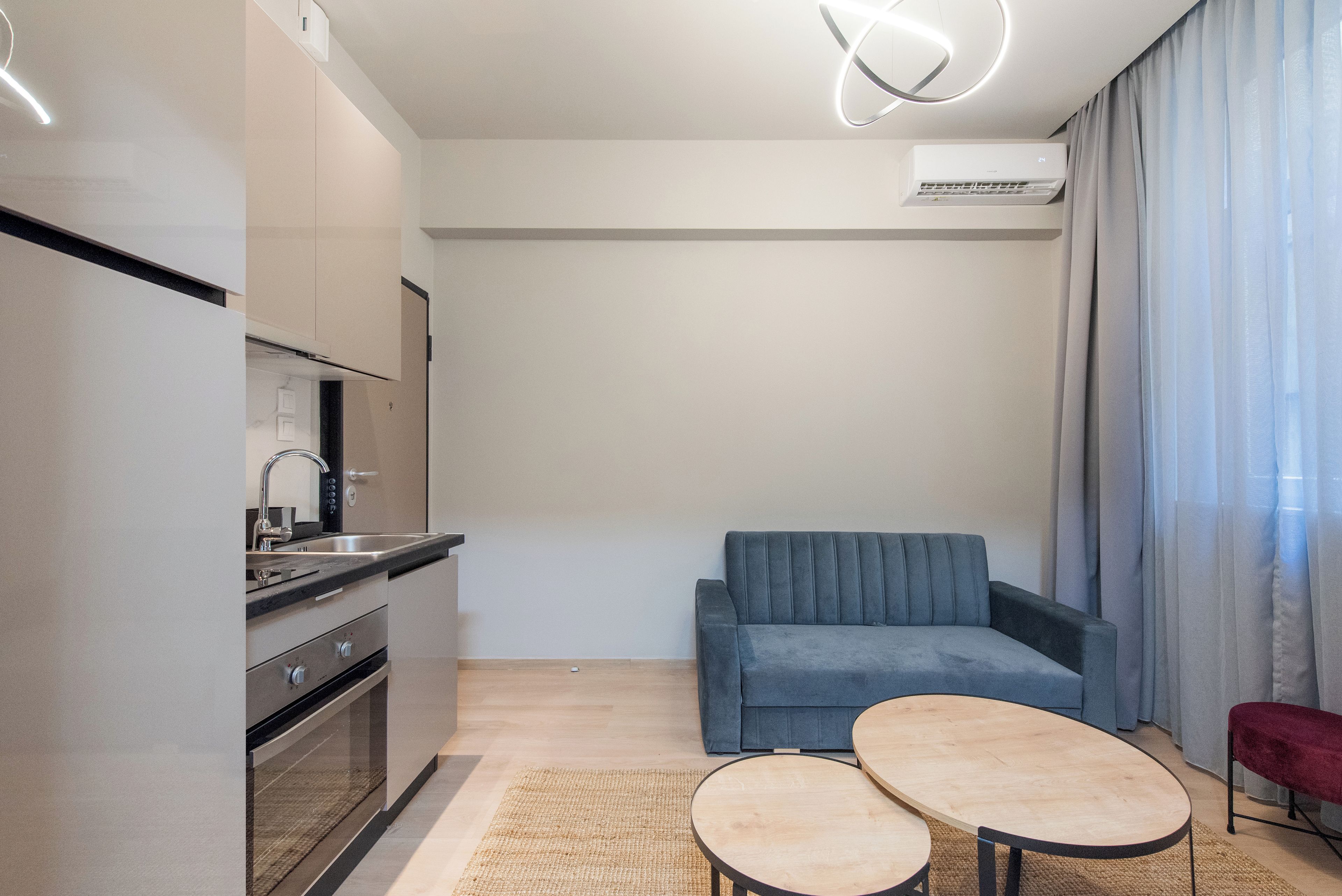 A modern kitchen with a built-in oven, a sink, and a dining area with a sofa and two small tables.