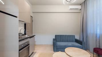 A modern kitchen with a built-in oven, a sink, and a dining area with a sofa and two small tables.