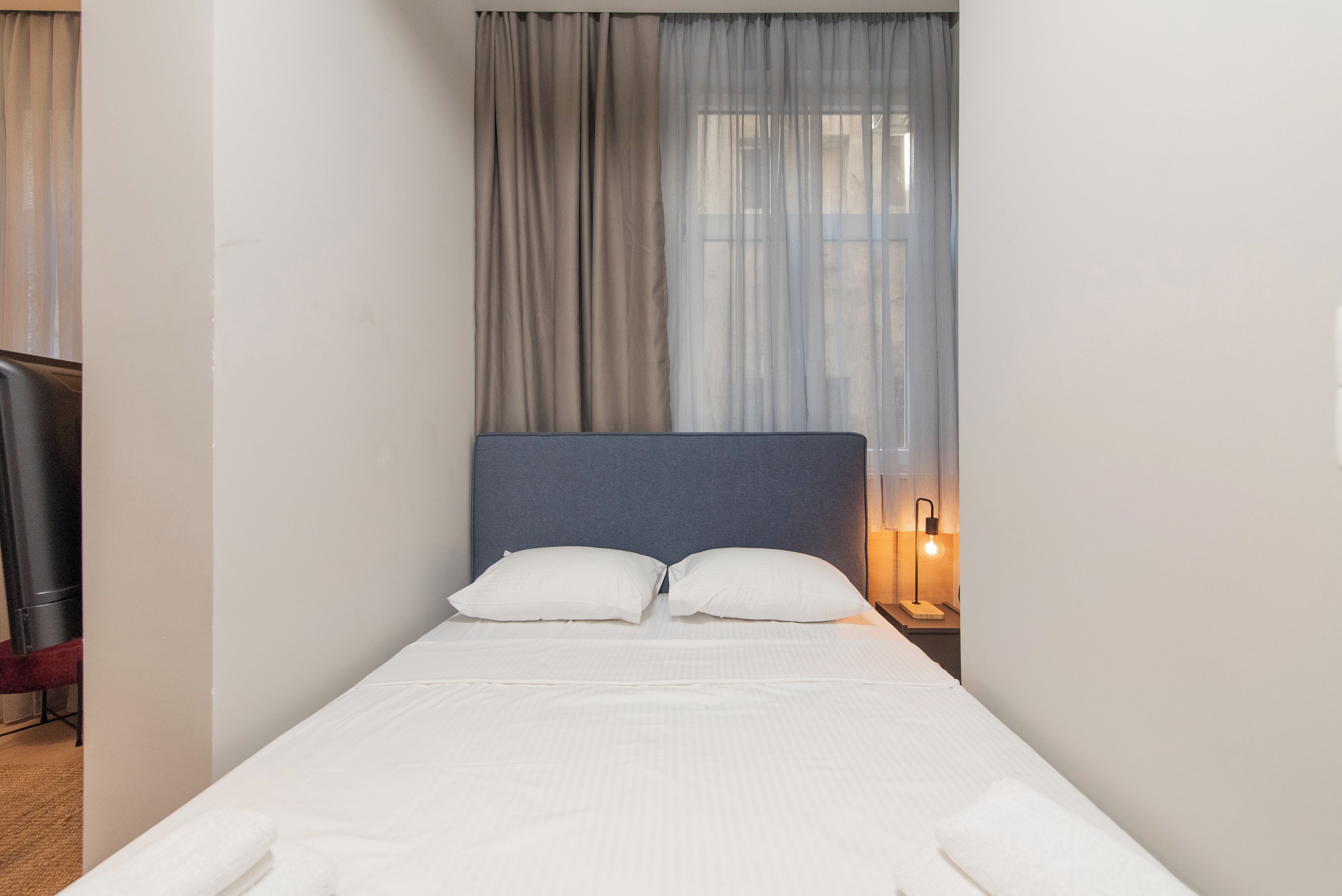 Una cama individual con cabecera, dos almohadas, una lámpara de noche y una ventana con cortinas.