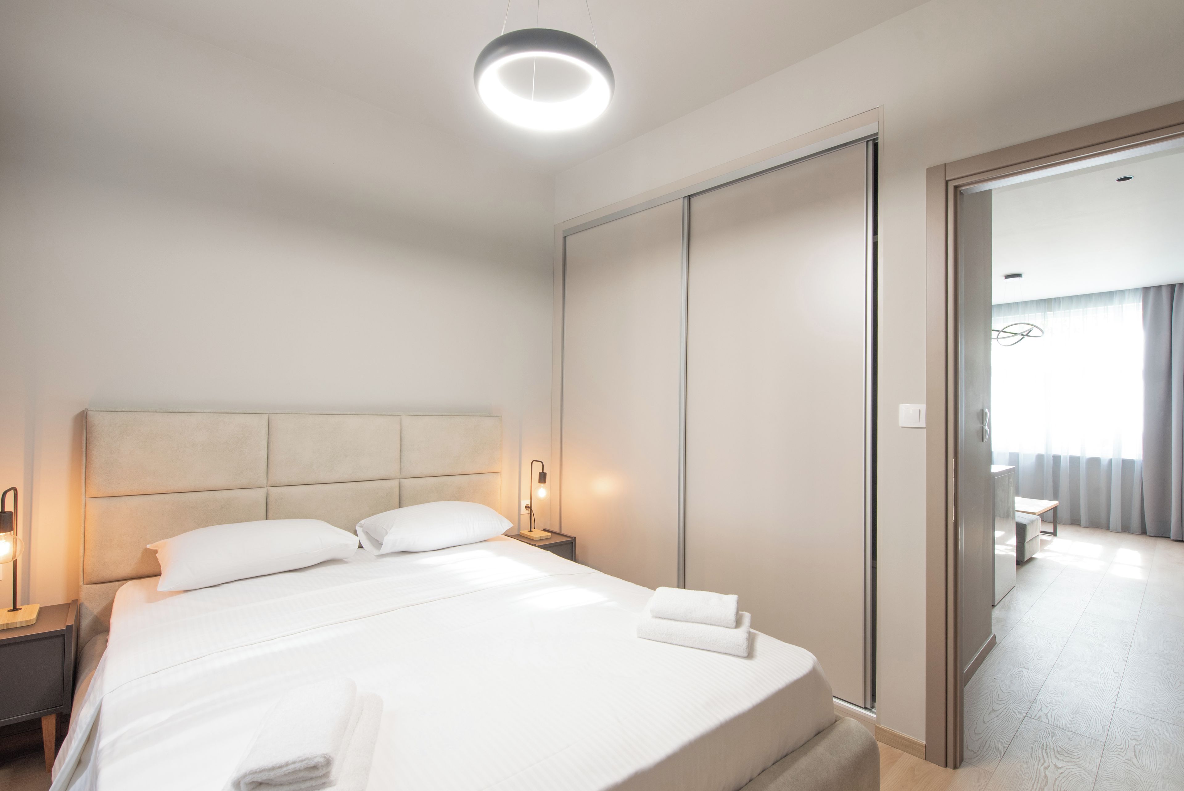 A hotel room with a large bed, bedside tables, a wardrobe, and a view of the adjacent room.