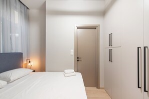 A modern hotel room with a neatly made bed, a bedside lamp, a door, and a wardrobe with two doors.