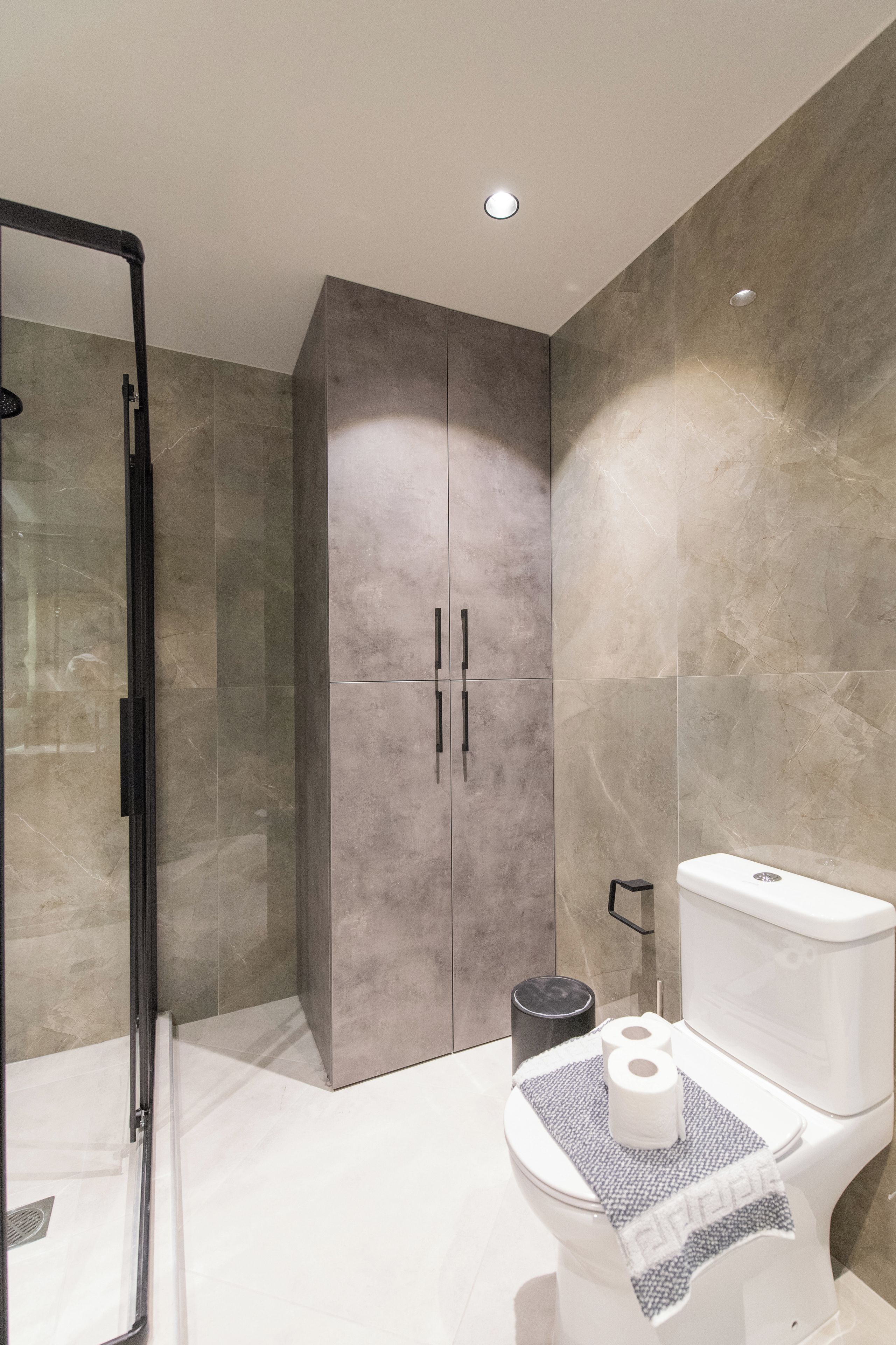 A modern bathroom with a glass shower enclosure, a toilet with a towel, and a large cabinet.