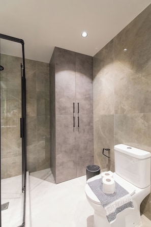 A modern bathroom with a glass shower enclosure, a toilet with a towel, and a large cabinet.