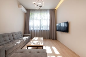 Una sala de estar moderna con sofá, una mesa de centro, televisor de pantalla plana y un amplio ventanal con cortinas.