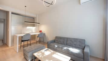 A modern living room with a grey sofa, a wooden coffee table, and a kitchen area with a white countertop and chairs.