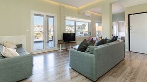 Un salon moderne avec un canapé gris, un téléviseur et une vue sur la ville grâce à de grandes fenêtres.