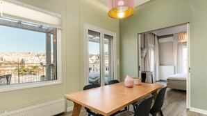 Un espace repas avec une table et des chaises en bois, une vue sur la ville grâce à de grandes fenêtres et un balcon doté d’une balustrade.