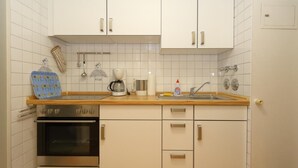 A kitchen with white cabinets, a stove, a sink, and a coffee maker. - House by the sea app. 071 WB (Westerland)