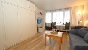 A modern living room with a sofa, a dining table with chairs, a TV, and a large wardrobe. - House by the sea app. 071 WB (Westerland)