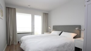 Une chambre d’hôtel moderne avec un grand lit, une table de chevet avec une lampe et une vue sur l’extérieur par la fenêtre.