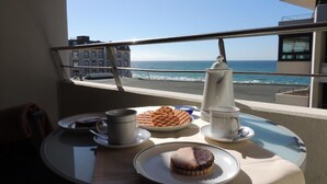 Un balcó amb una taula preparada per esmorzar, amb vista a una platja i l'oceà.