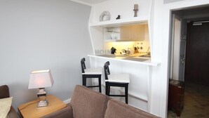 Ein kompakter Wohnraum mit Küchenzeile, einer kleinen Essecke mit zwei Stühlen, einer Lampe und einem Sofa.