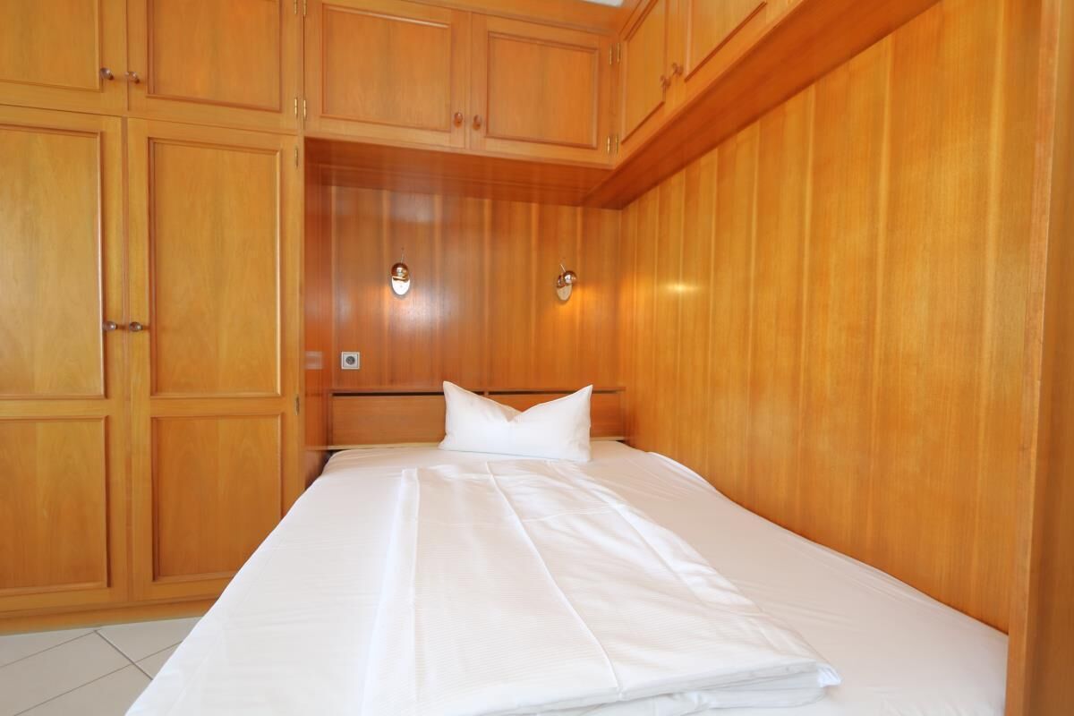 A hotel room with wooden paneling, a bed with white linens, and two wall-mounted light fixtures.