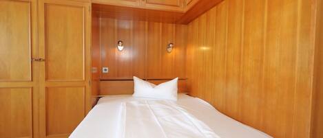 A hotel room with wooden paneling, a bed with white linens, and two wall-mounted light fixtures.