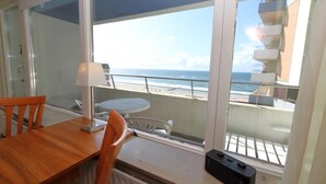 Un balcon avec vue sur la plage et l’océan, une table en bois, une chaise et une lampe.