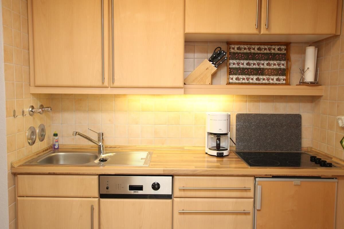 Una cocina compacta con un lavamanos, una cafetera y un juego de cuchillos en la encimera.