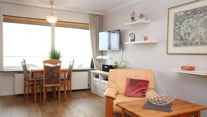A living room with a wooden dining table, chairs, a sofa, a TV, and decorative items on shelves. - House by the sea app. 105 WB (Westerland)