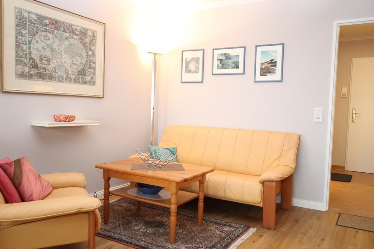 A living room with a yellow sofa, a wooden coffee table, a framed map, and three framed pictures on the wall.