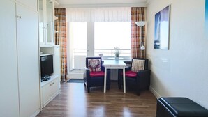 A compact living space with a kitchenette, a dining area with two chairs, a television, and a window with curtains. - Haus am Meer, App. 139 a <br>Location:<br>The apartment with west-facing balcony and sea view is located on the 7th floor of a well-kept apartment building in the resort center, directly on the main beach. The house is centrally located in Westerland, bet (Westerland)