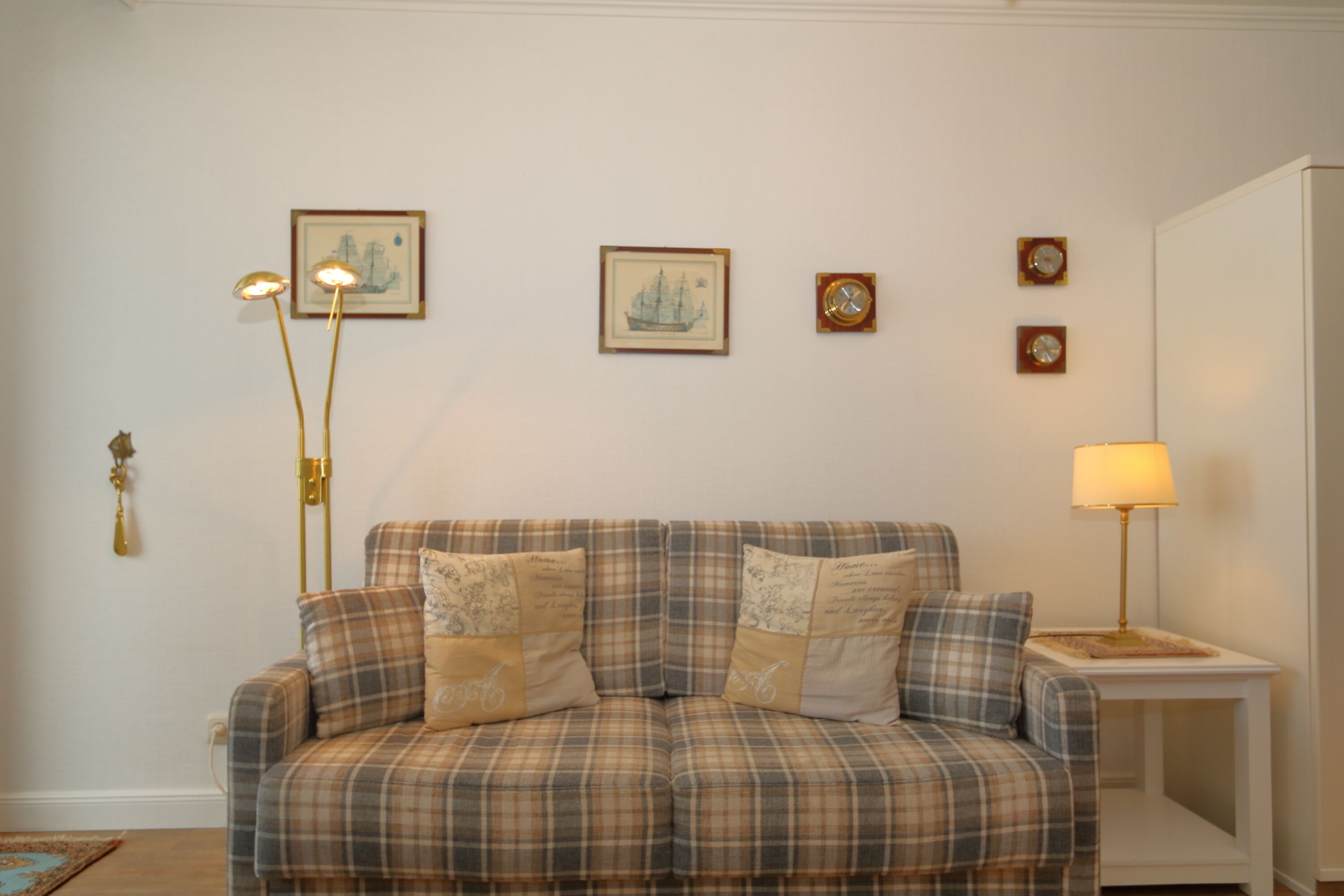 A plaid sofa with decorative pillows, a floor lamp, and framed artwork on the wall.