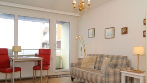 Un salon avec un canapé à carreaux, des fauteuils rouges, une petite table et un lustre.