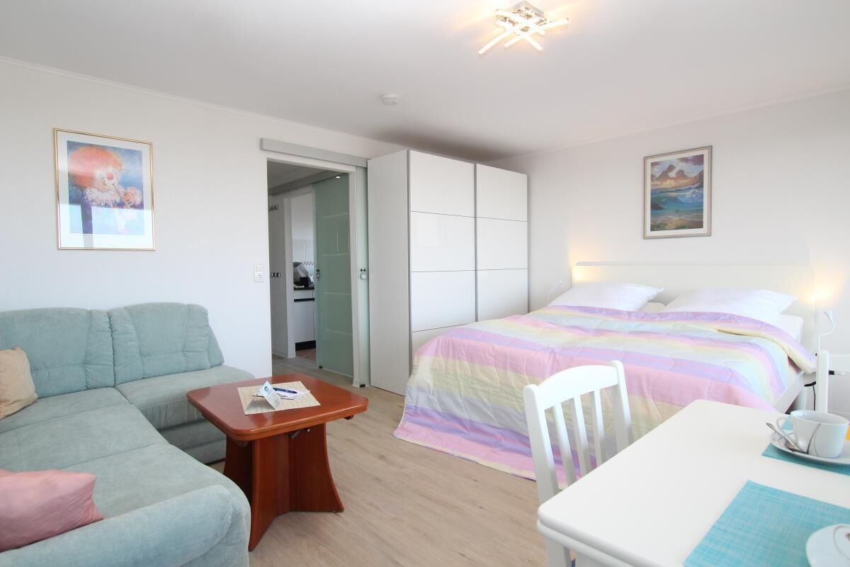 A bedroom with a bed, a bedside table, a chair, a sofa, and a small table.