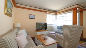 Une chambre d’hôtel avec un canapé à rayures, une table basse en bois, un téléviseur et un fauteuil à rayures.