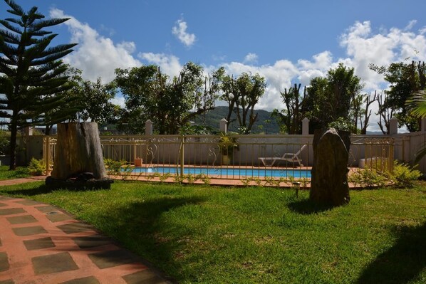A pool area with a fence, lounge chairs, and a pathway.