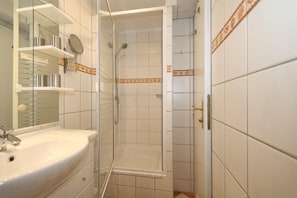 Bathroom features a sink, mirror, and shower with a glass door and showerhead.