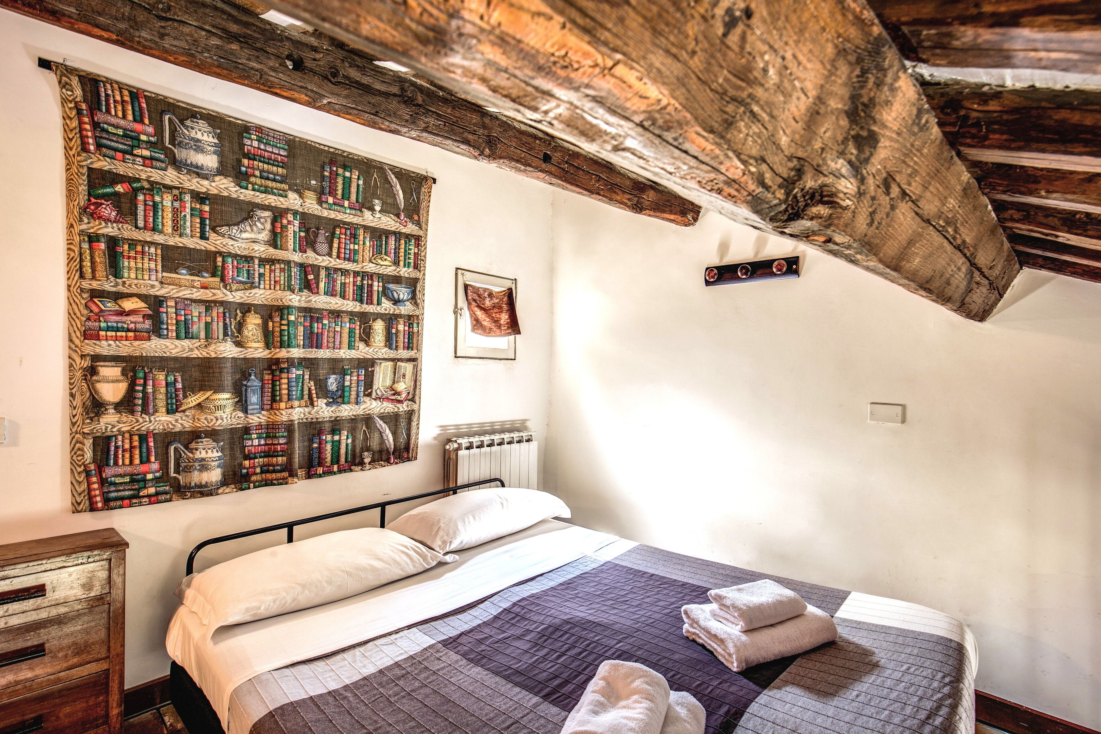 A bedroom with a large bookshelf, a bed with a quilt, and a rustic wooden ceiling.