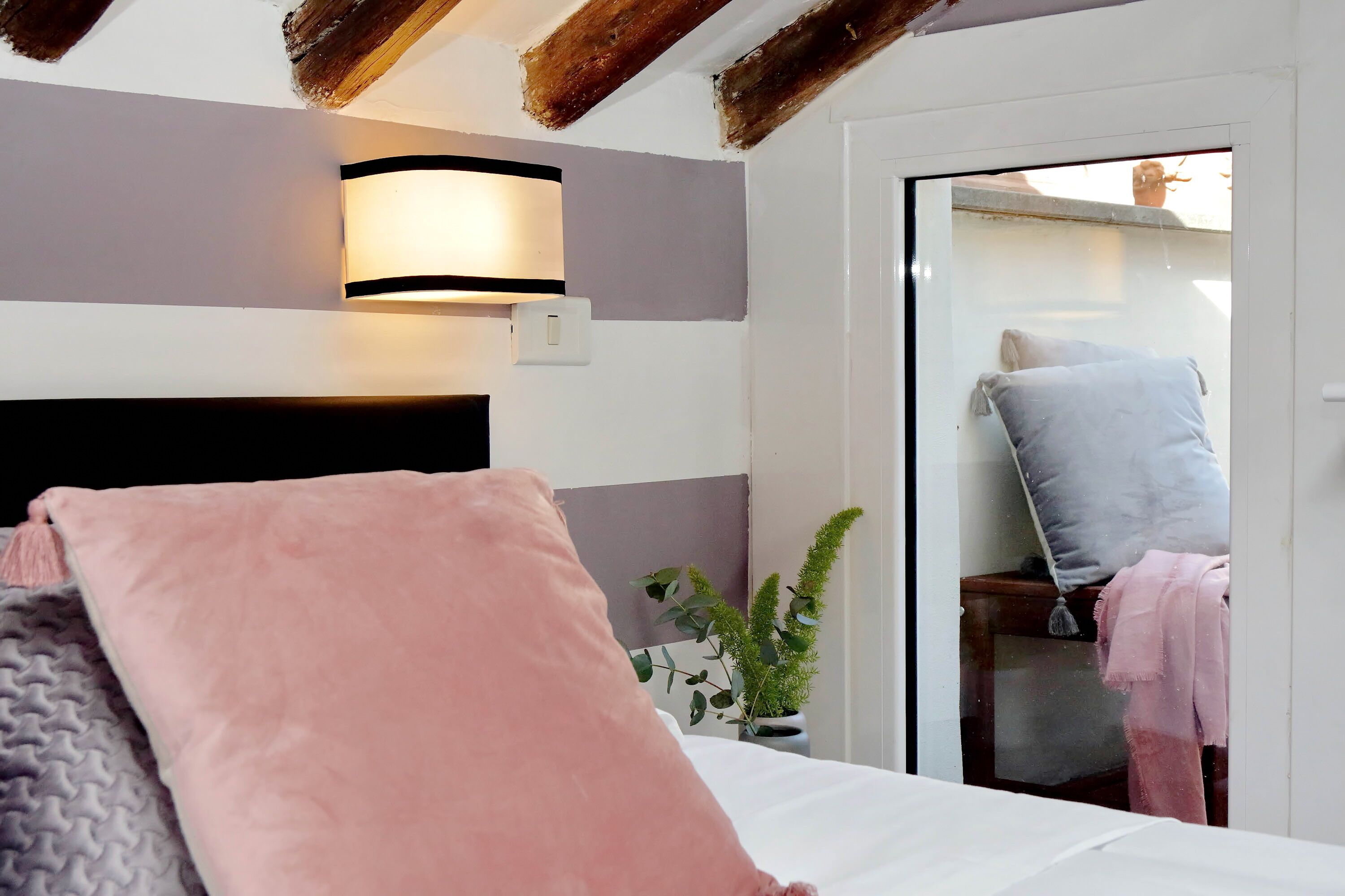 Een slaapkamer met een bed, een bedlamp, een kamerplant en een schuifdeur naar een buitenruimte.