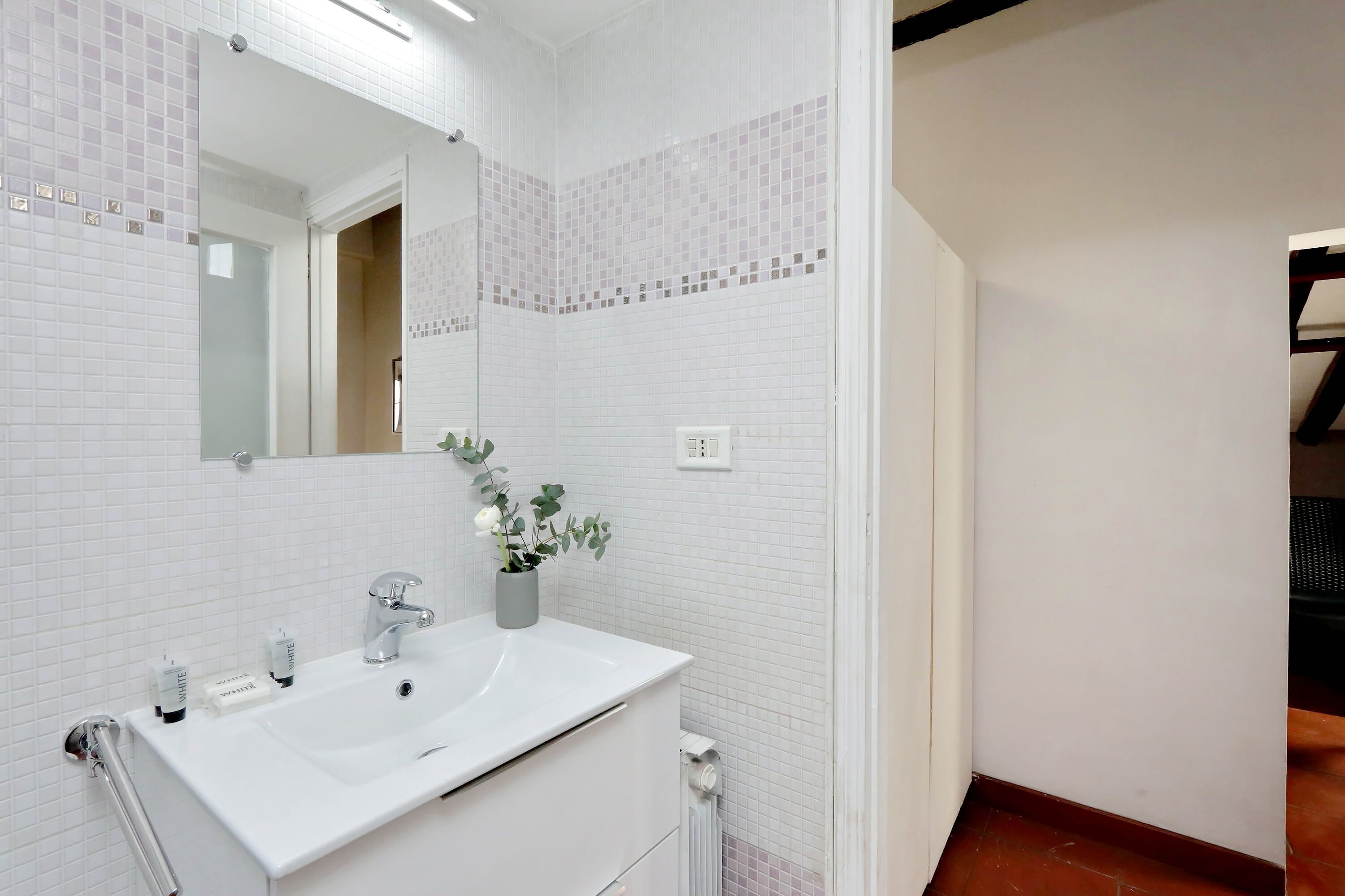 Une salle de bain moderne avec des murs recouverts de carreaux blancs, un lavabo blanc et un miroir au-dessus.
