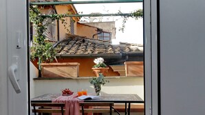 Ein Balkon mit Tisch für zwei Personen, einem Blumentopf und Blick auf traditionelle Ziegeldächer.