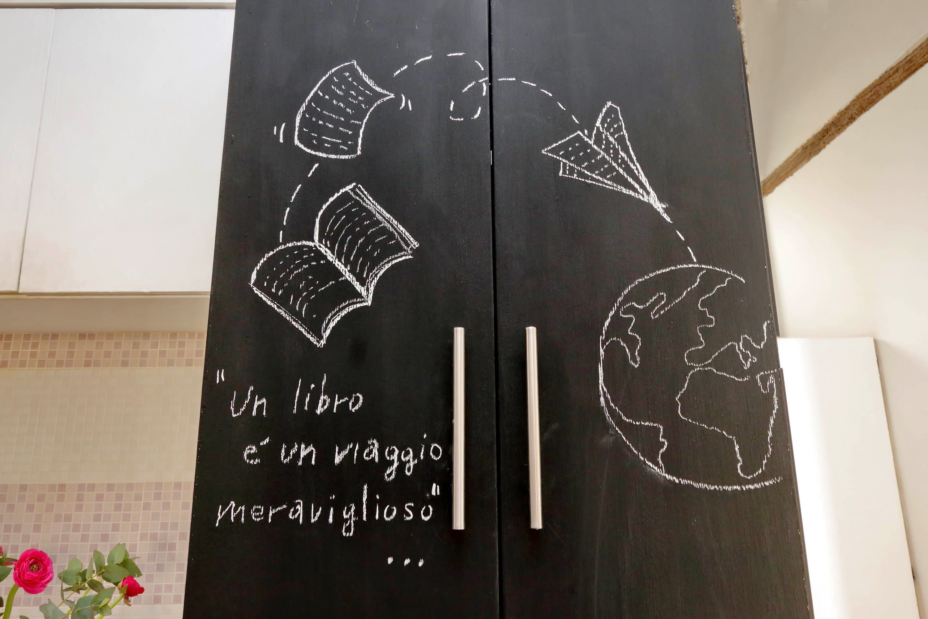 A blackboard with drawings of a globe, books, and a paper airplane, along with a quote in Italian.