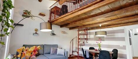 A cozy living area with a sofa, dining table, chairs, and a staircase with a wooden railing.