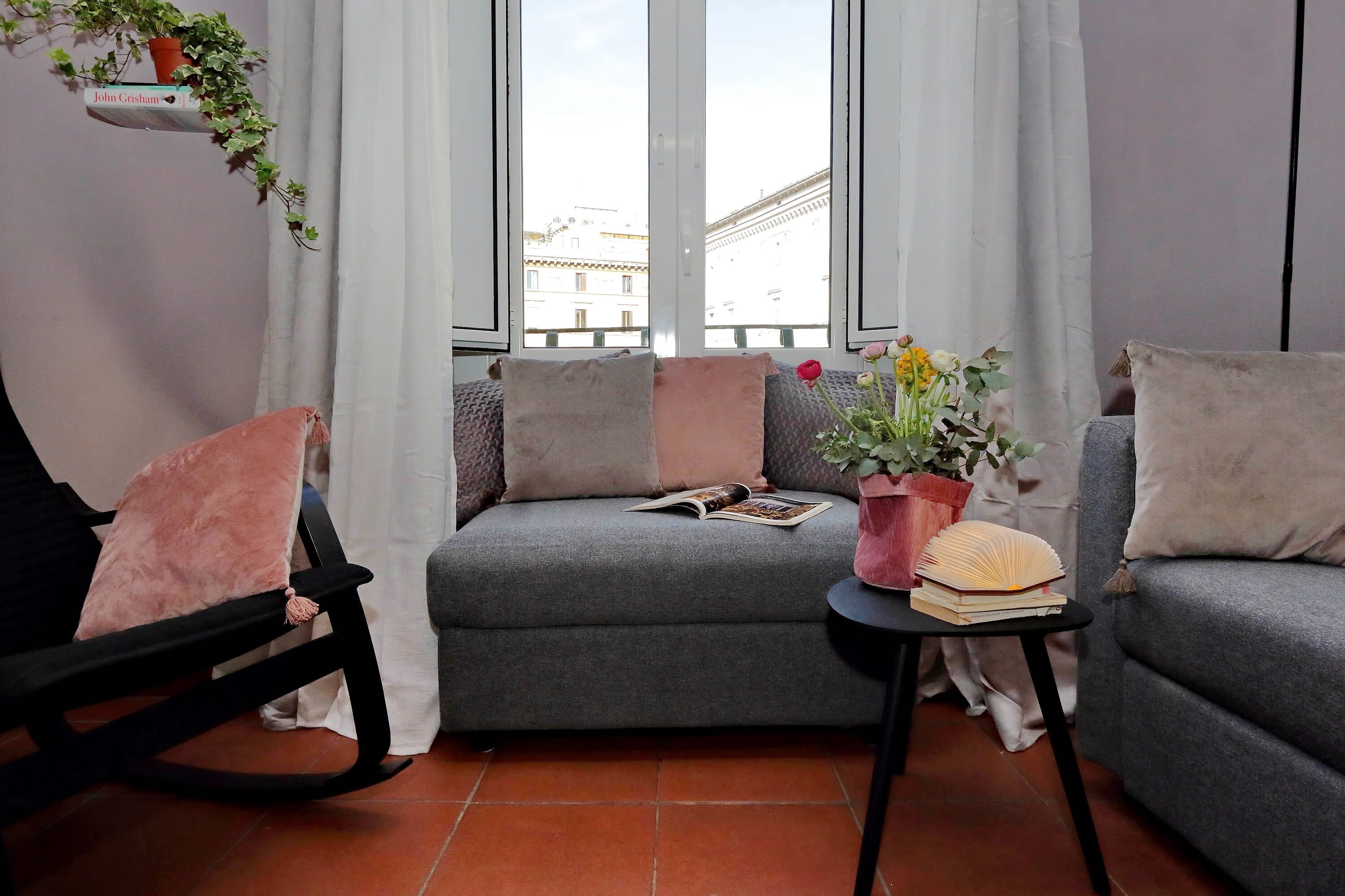 A cozy living room with a grey sofa, a black rocking chair, and a small table with a book and a potted plant.