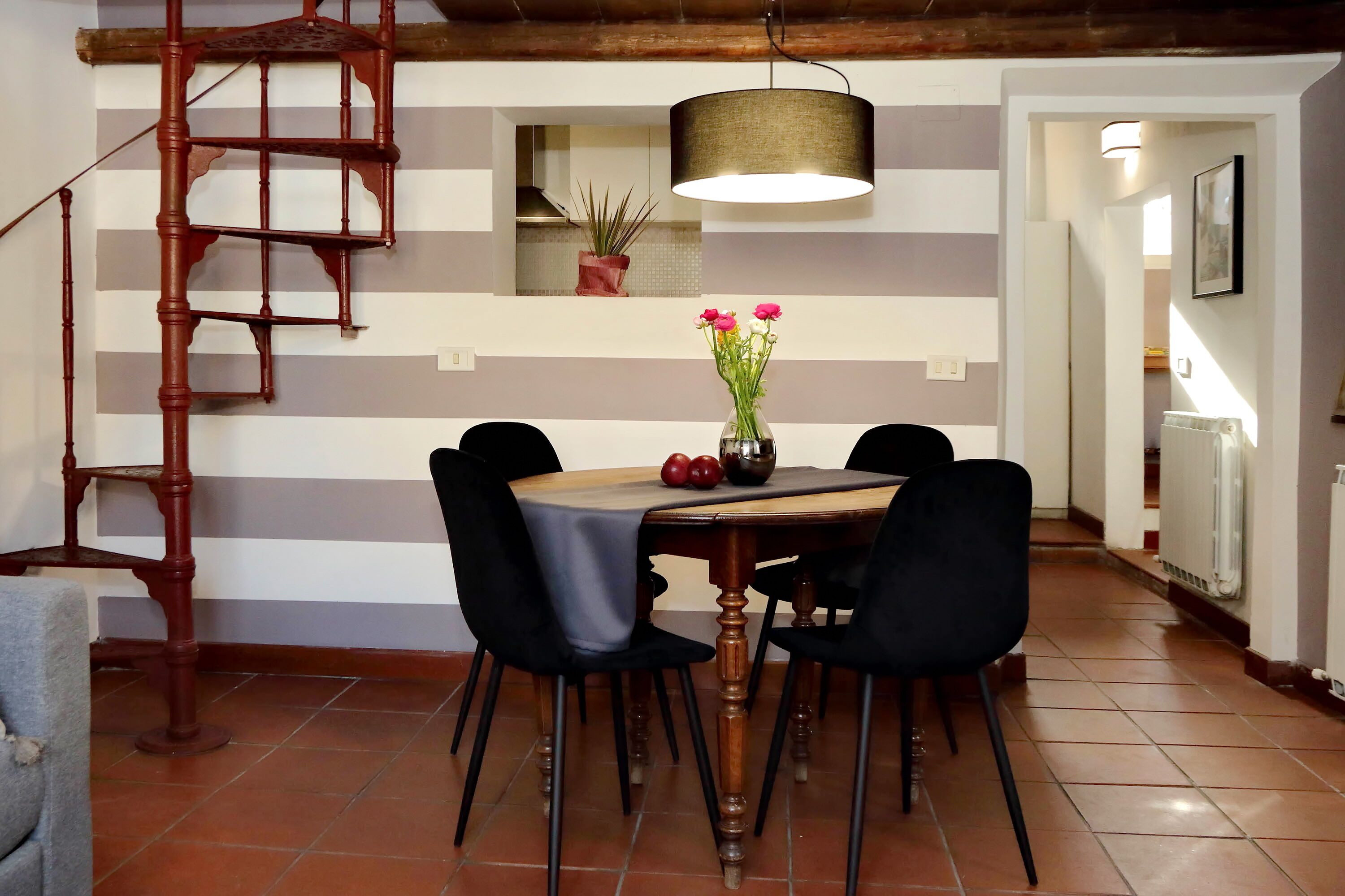 A dining area with a wooden table, four chairs, a vase with flowers, and a hanging lamp.