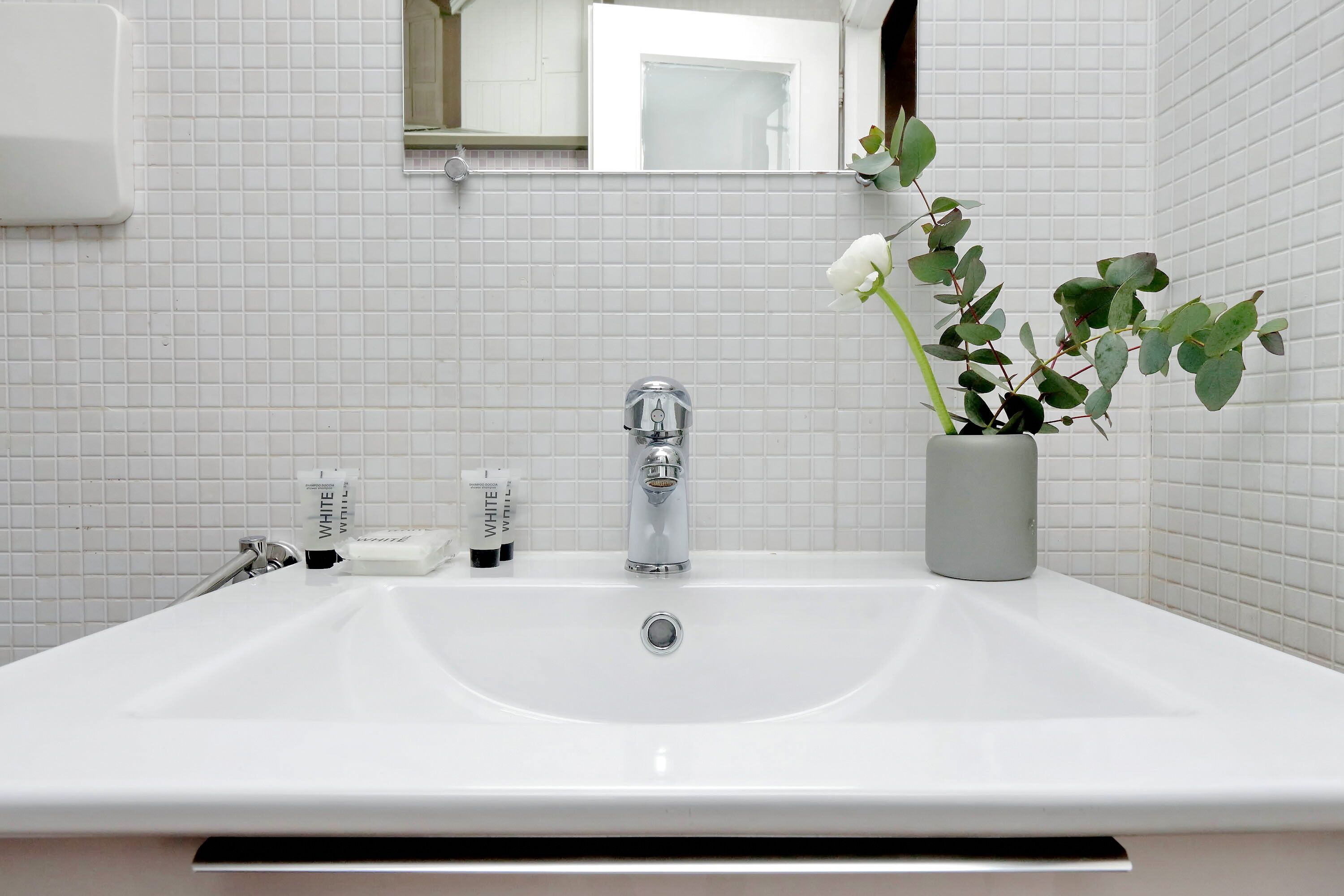 Een wit wastafelmeubel met een spiegel erboven, een potplant en toiletartikelen op het aanrecht.