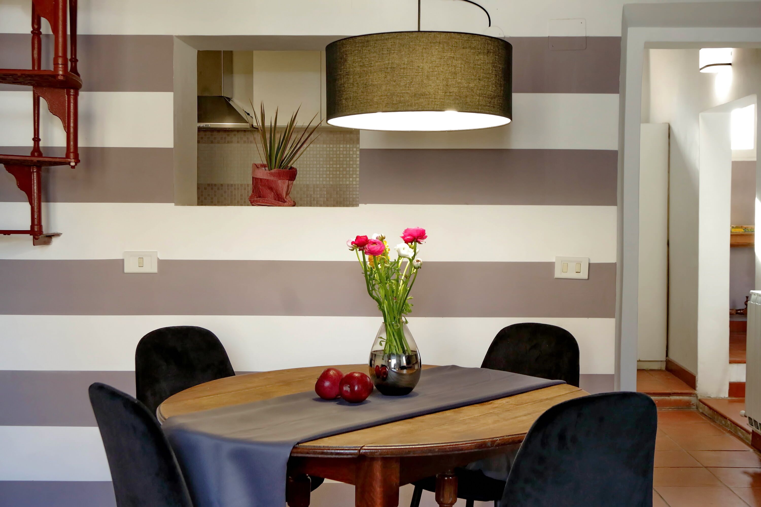 En spiseplads med et træbord, sorte stole, en vase med blomster og en hængende lampe.