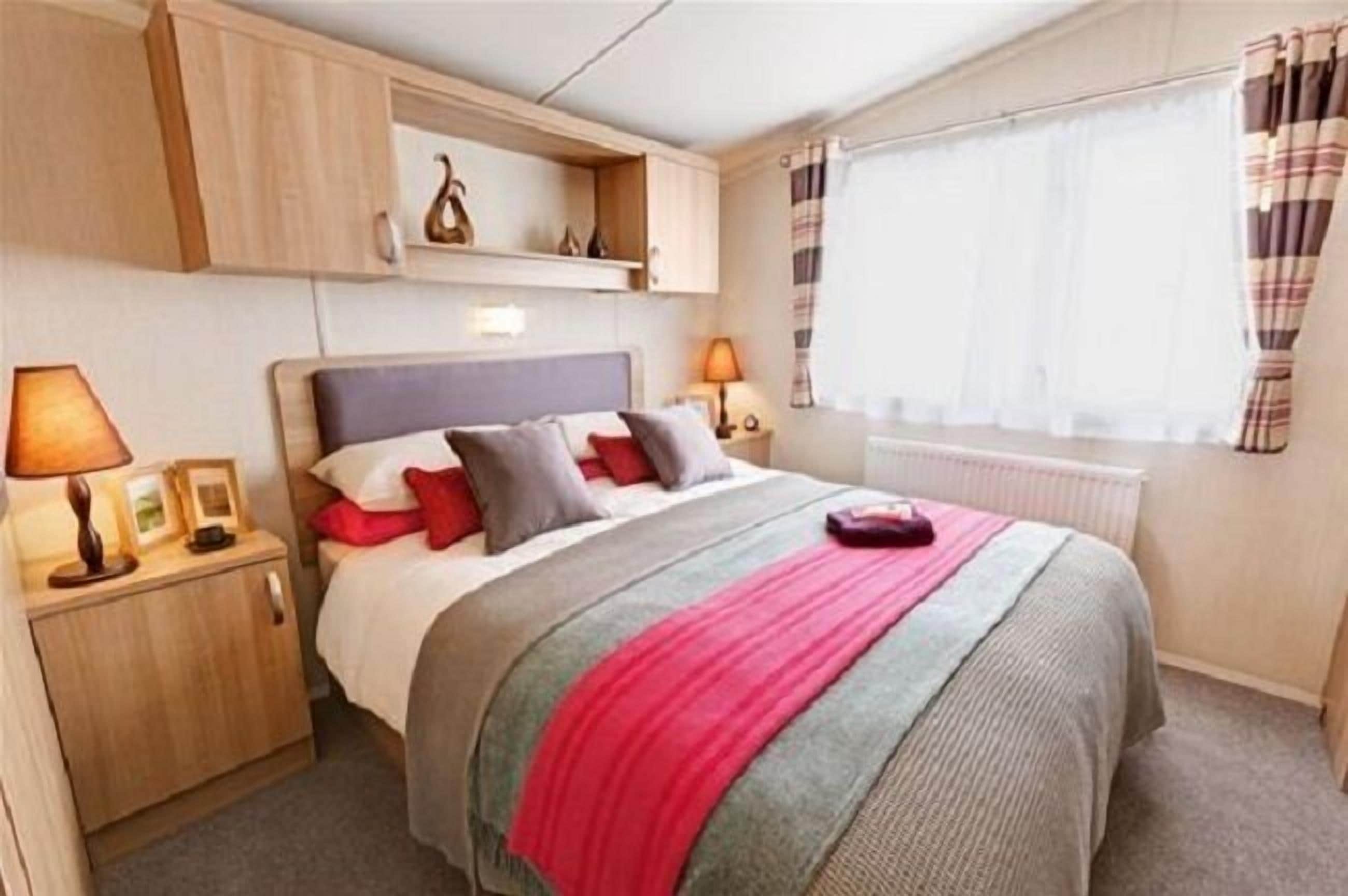 Quarto com cama, mesas de cabeceira, guarda-roupa e janela com cortinas.