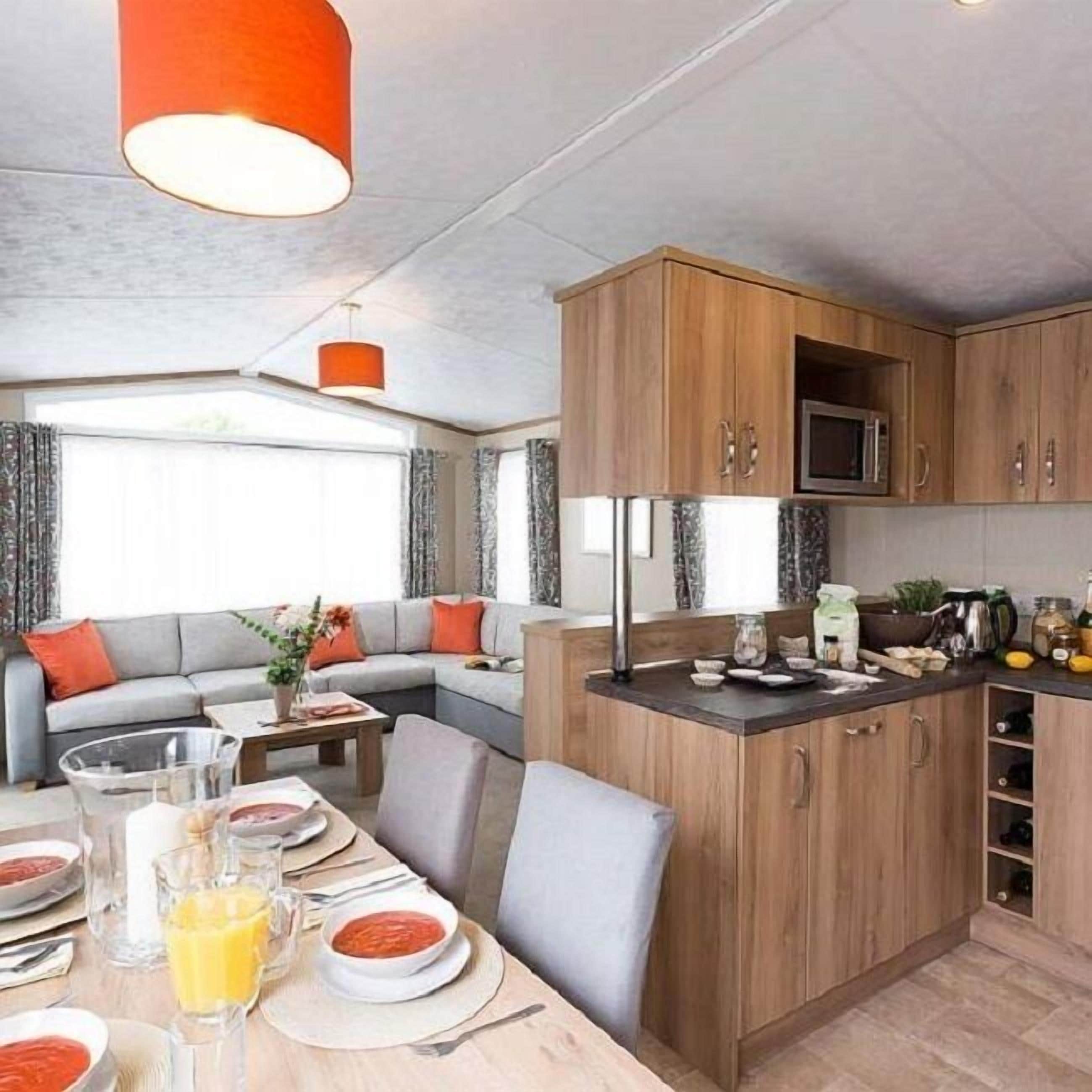 A modern kitchen with wooden cabinets, a microwave, and a dining area with a table set for two.