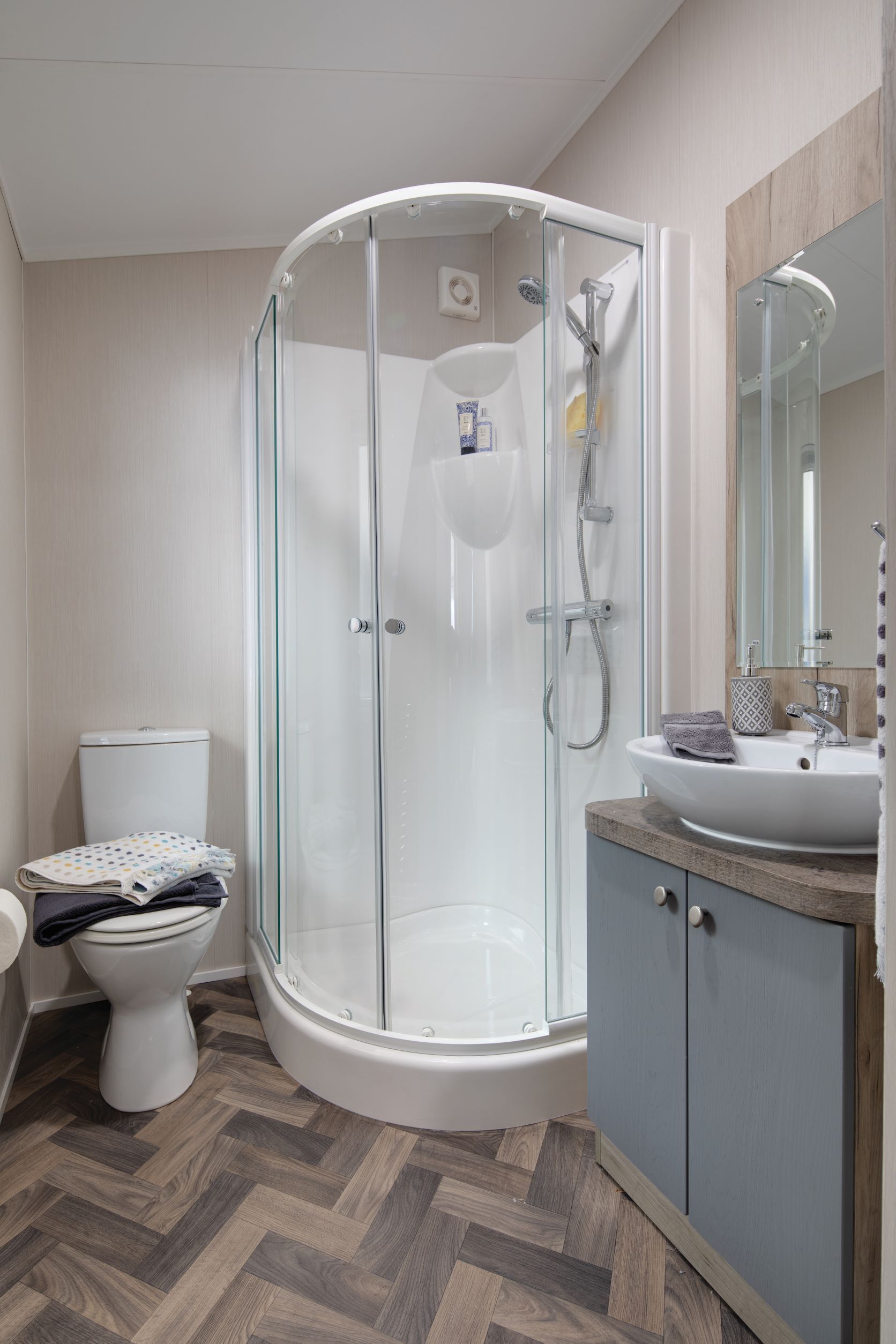 A modern bathroom with a glass-enclosed shower, a toilet, and a sink with a mirror above it.