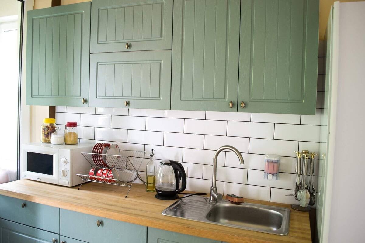 A kitchen with teal cabinets, a white microwave, a sink, and various kitchen utensils.